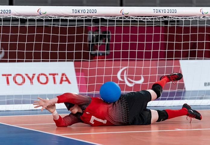 A female athlete blocks a blue ball in front of the net during a goalball game. 