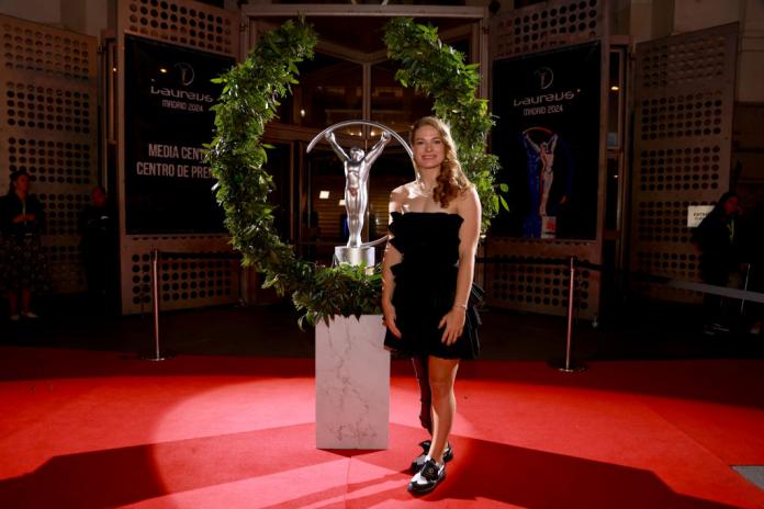 A female athlete poses for a photo in front of a Laureus Award trophy