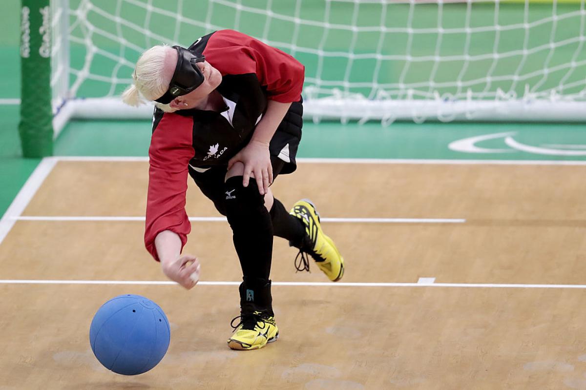 A female athlete throws a blue ball in front of the net during a goalball game. 